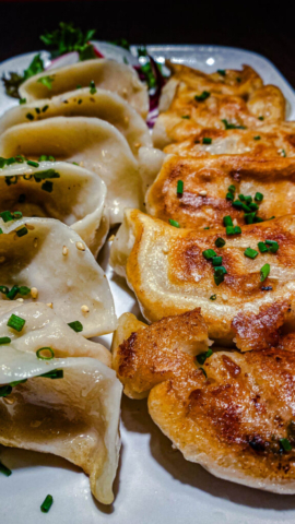 A close-up of freshly made pan-fried dumplings, garnished with sesame seeds and chopped chives.