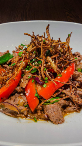 A vibrant beef stir-fry with tender beef slices, crisp red bell peppers and sliced ginger. Garnished with sesame seeds and fresh herbs.